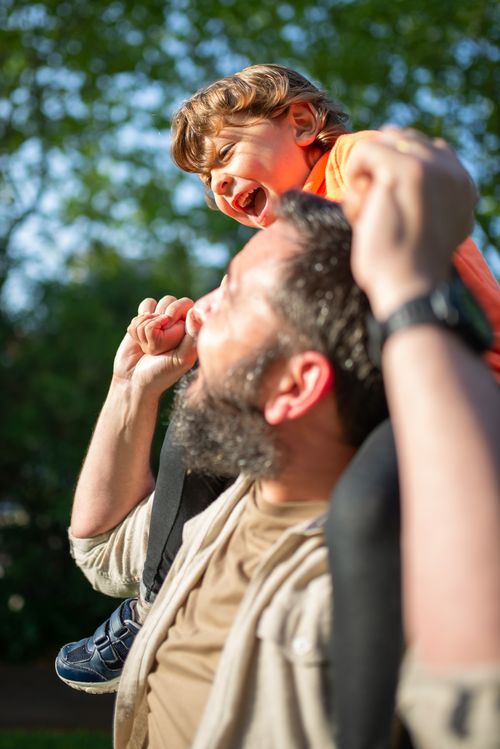 Free Father giving son a piggyback ride, sharing laughter in a sunny park setting. Stock Photo