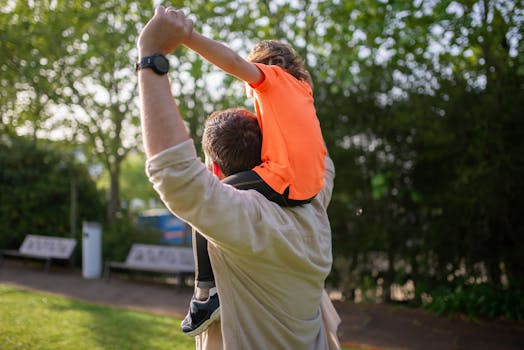 A joyful father carrying his son on his shoulders in a lush park setting, embodying family bonding and playful fun.