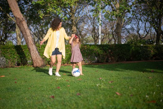 A mother and daughter enjoying a sunny day playing soccer in a lush green park.