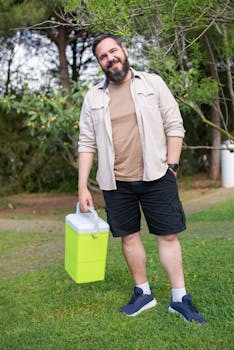 Smiling man with a beard holding a cooler outdoors. Casual and relaxed setting.