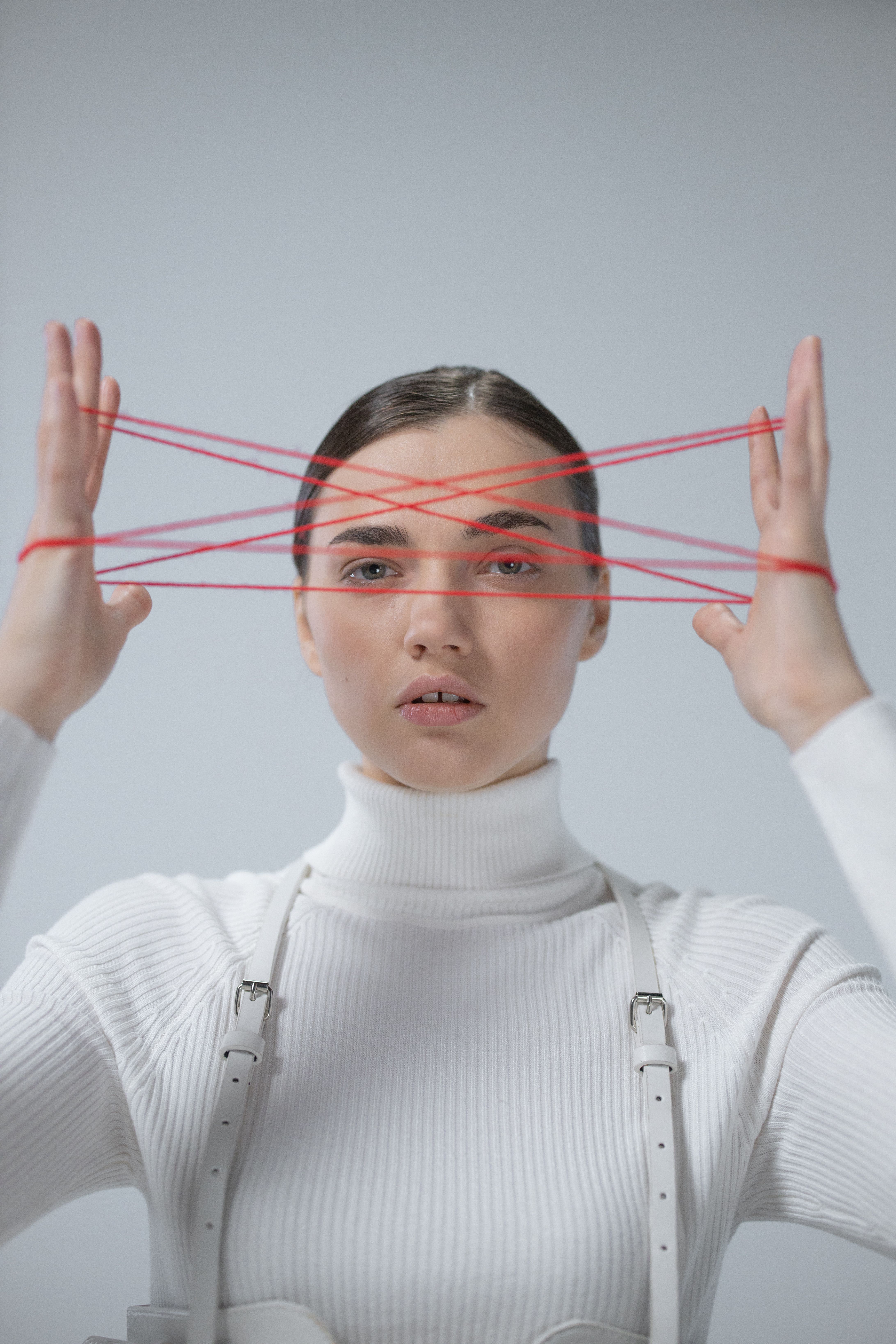 Woman in white turtleneck playing string game with red threads. Conceptual portrait with modern style.