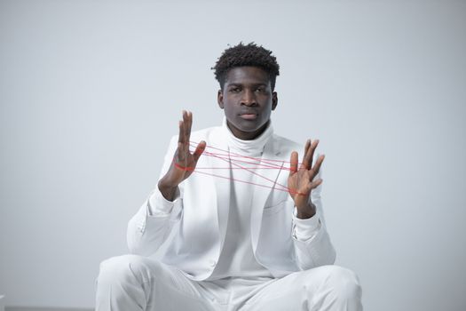 Elegant portrait of a man in a white suit playing with red string art against a minimalistic background.