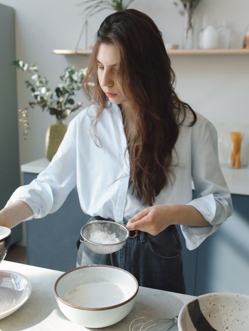 Free A woman sifting flour in a contemporary kitchen setting, showcasing culinary preparation. Stock Photo