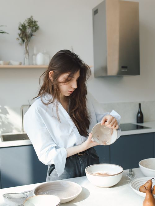 Free A young woman pours ingredients into a bowl in a bright, modern kitchen. Stock Photo