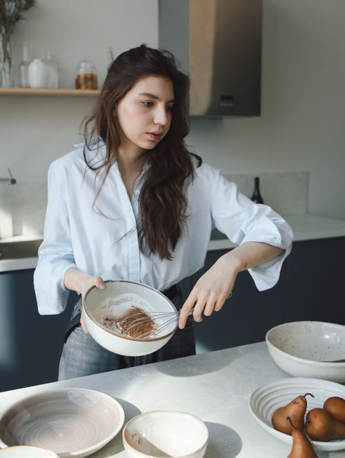 Free Woman mixing ingredients in a bowl in an airy, modern kitchen setting. Stock Photo