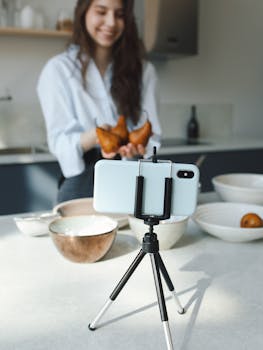 A woman holds pears while recording a cooking video in a stylish kitchen with a smartphone.