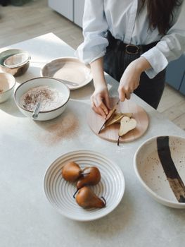 A woman slicing pears on a wooden board in a contemporary kitchen with ceramic dishes.