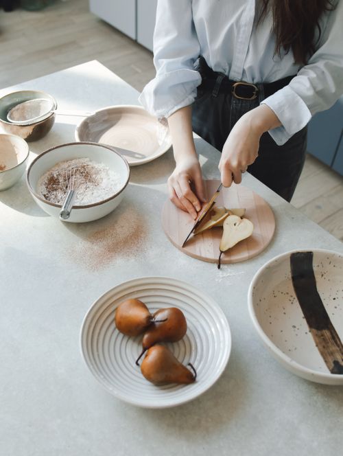 Free A woman slicing pears on a wooden board in a contemporary kitchen with ceramic dishes. Stock Photo