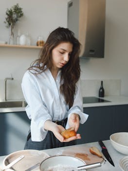 Young woman preparing food in a modern kitchen with natural light and utensils around.