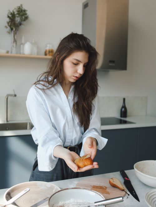 Free Young woman preparing food in a modern kitchen with natural light and utensils around. Stock Photo