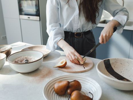 A woman slicing a pear in a modern kitchen setting, ready for baking.