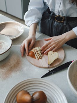 Person slicing pears on a wooden board for baking in a cozy kitchen setting.