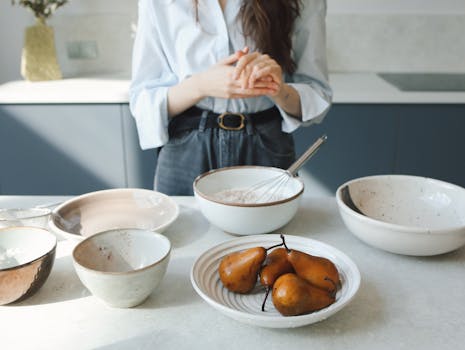 Woman mixing ingredients in a modern kitchen with pears and bowls, creating an inviting culinary scene.