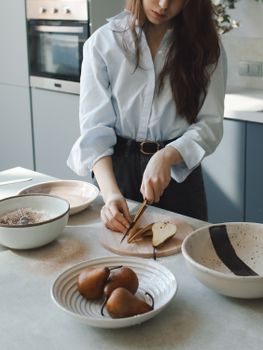 Young woman preparing pears in a stylish kitchen, showcasing a minimalist interior and food preparation.