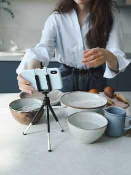 Woman preparing ingredients for a cooking video tutorial using a smartphone on a tripod.