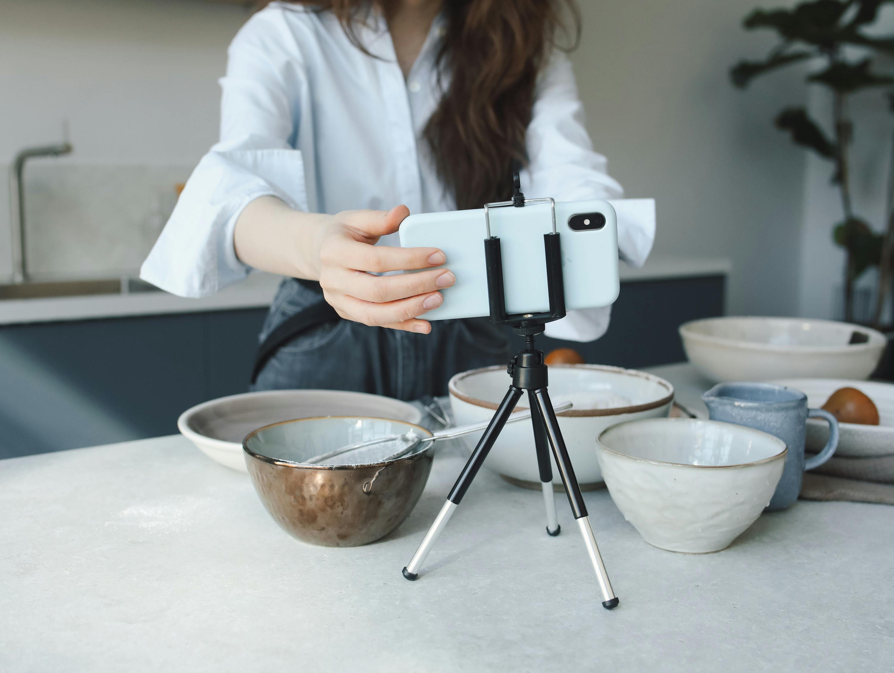 Woman using a smartphone on a tripod for vlogging in the kitchen with bowls