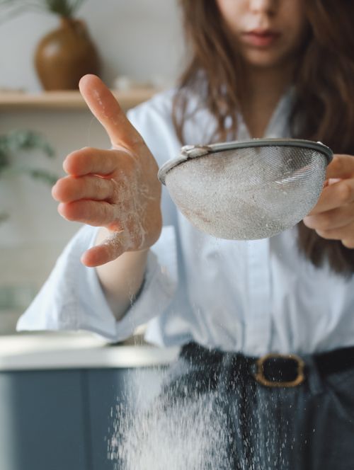 Free Close-up of a woman sifting flour in a bright kitchen, capturing a moment of domestic baking. Stock Photo