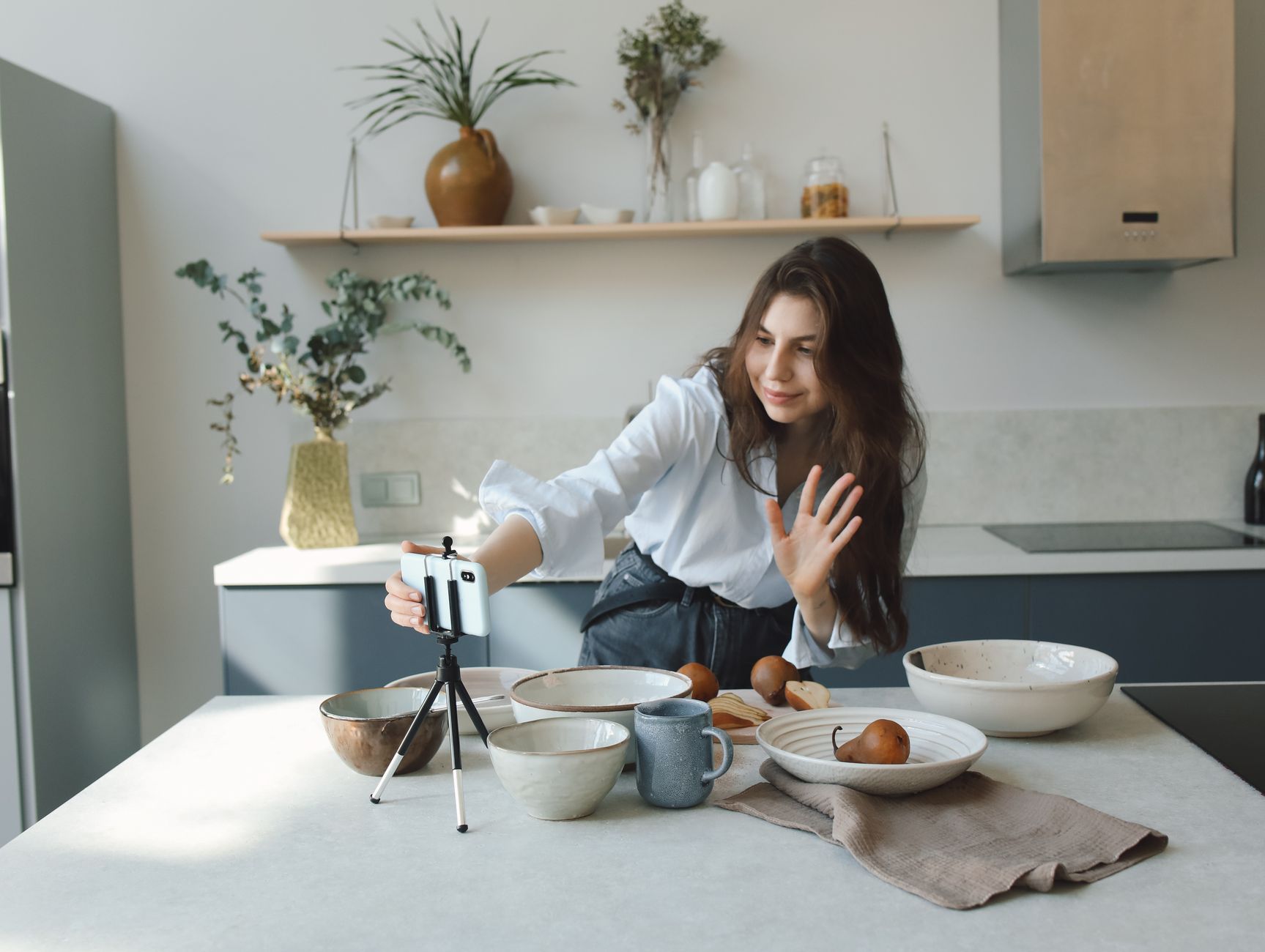 Woman filming cooking video in modern kitchen with smartphone and tripod. Bright and casual atmosphere.
