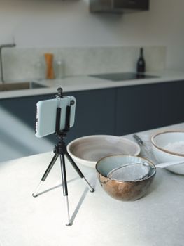 A modern kitchen setup featuring bowls and a smartphone on a tripod for recording recipes.
