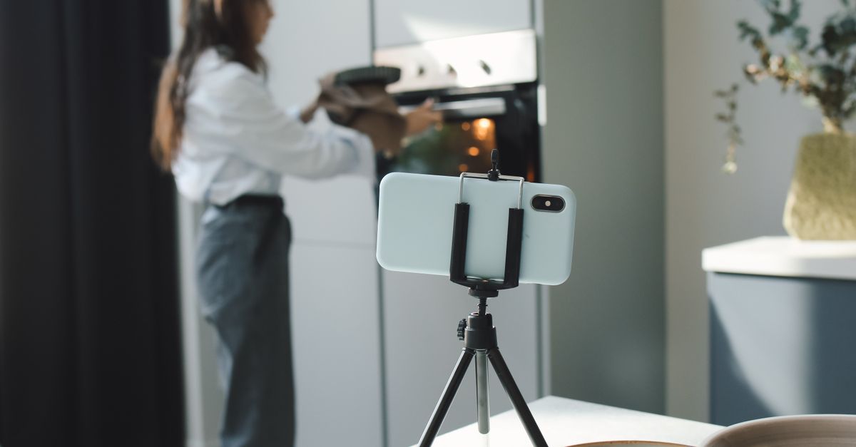 A woman uses a smartphone on a tripod to film her baking process in a modern kitchen.