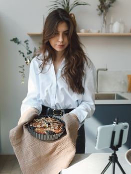 Young woman holding freshly baked goods, filmed in a modern kitchen setting.