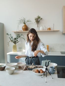 Young woman baking in a modern kitchen, filming content for her vlog.