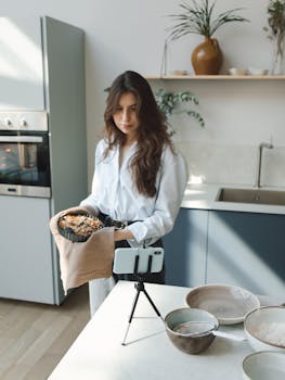 Woman vlogging while cooking in a modern kitchen setting.