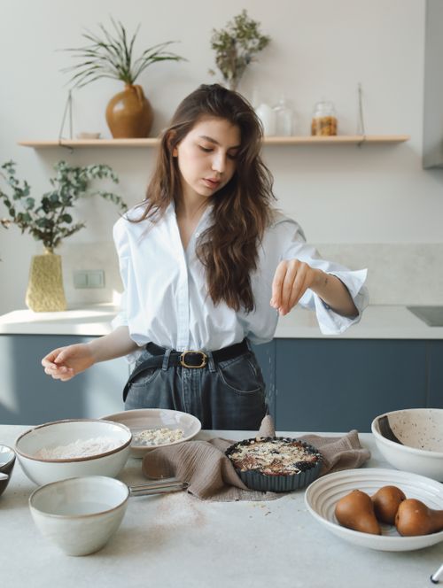 Free A young woman sprinkles ingredients on a tart in a stylish, modern kitchen setting. Stock Photo