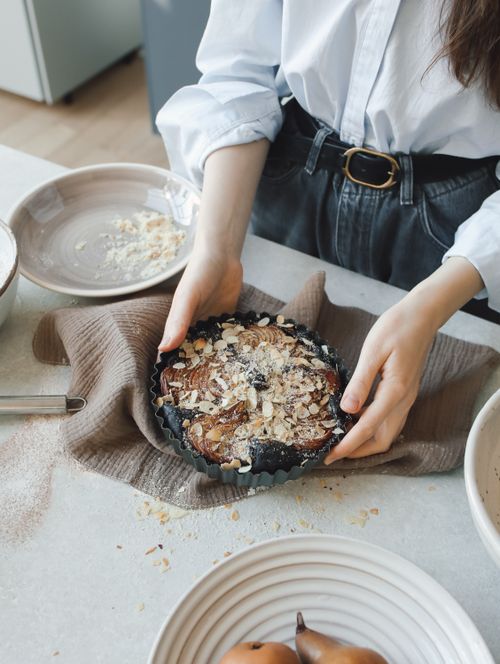 Free Woman prepares a homemade fruit tart with almonds and berries in an inviting kitchen setting. Stock Photo