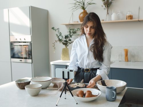 Free A woman cooking in a stylish kitchen while recording a vlog. Stock Photo