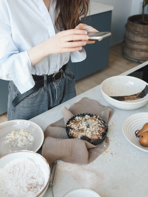 Free Young woman taking a smartphone photo of a homemade pie in a modern kitchen setting. Stock Photo