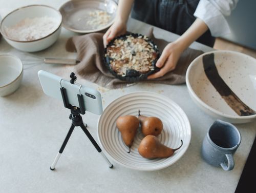 Free Woman baking in kitchen while recording with smartphone, showing delicious pears and a cake. Stock Photo