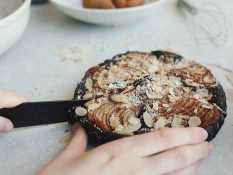 Close-up of a hand slicing a homemade almond pear tart on a table.