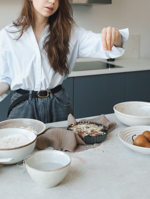 Free A woman in a stylish kitchen sprinkles ingredients on a freshly baked dessert. Stock Photo