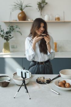 Smiling woman filming herself enjoying a delicious dessert in a stylish kitchen.