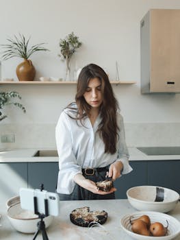 Woman baking in kitchen, recording cooking video for vlog. Modern culinary setup.
