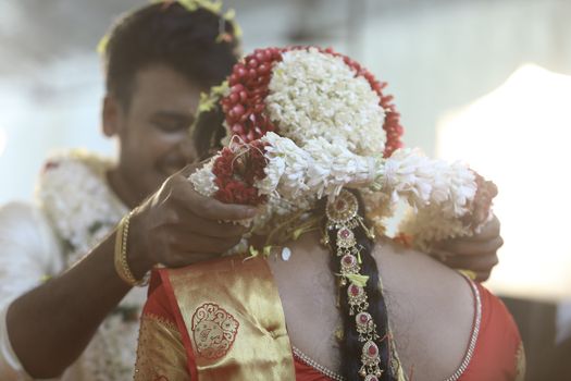 A groom places a floral garland on the bride during a traditional South Indian wedding ceremony.