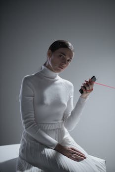 Elegant woman in a white sweater and skirt holding a red laser pointer against gray background.