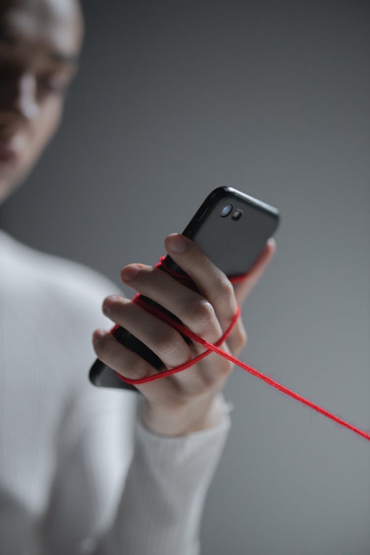 Person Holding Black Phone With Red String