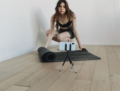 A woman prepares her yoga mat for an indoor workout session, focusing on wellness and fitness.
