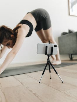 Woman practicing yoga indoors with smartphone streaming her session.