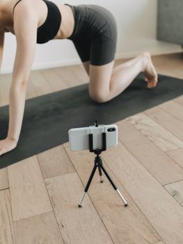 Woman practicing yoga indoors while recording with smartphone on tripod.