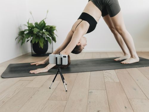 Free Woman practicing yoga poses on a mat with a smartphone for online tutorial. Stock Photo