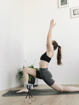 Woman in yoga pose indoors using smartphone for remote yoga session, promoting wellness and fitness.