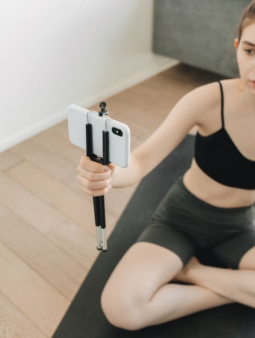 Free Young woman records yoga practice using smartphone and tripod indoors, emphasizing fitness lifestyle. Stock Photo