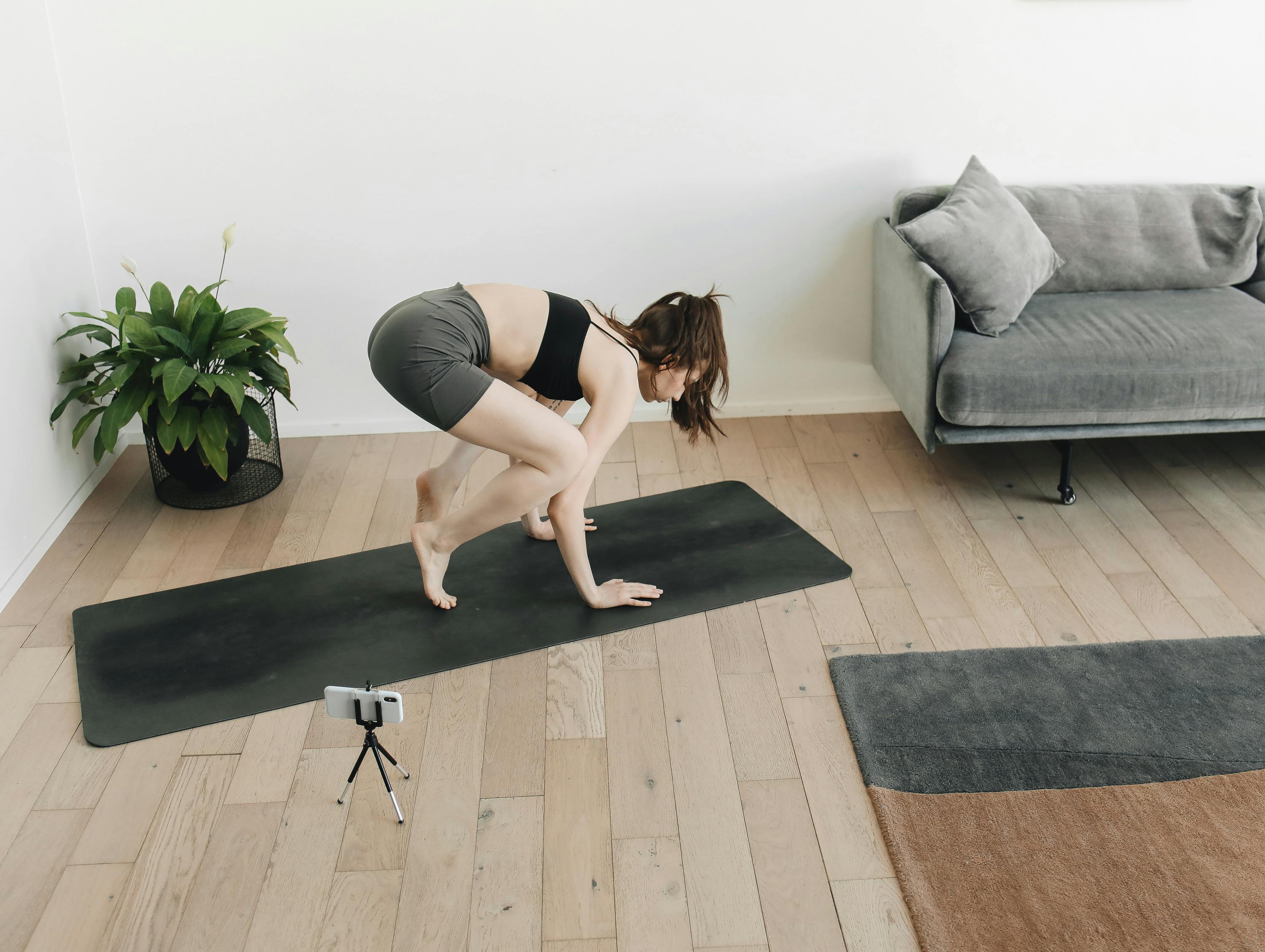 Woman practicing yoga at home on a mat with a smartphone recording. Ideal for fitness and lifestyle themes.