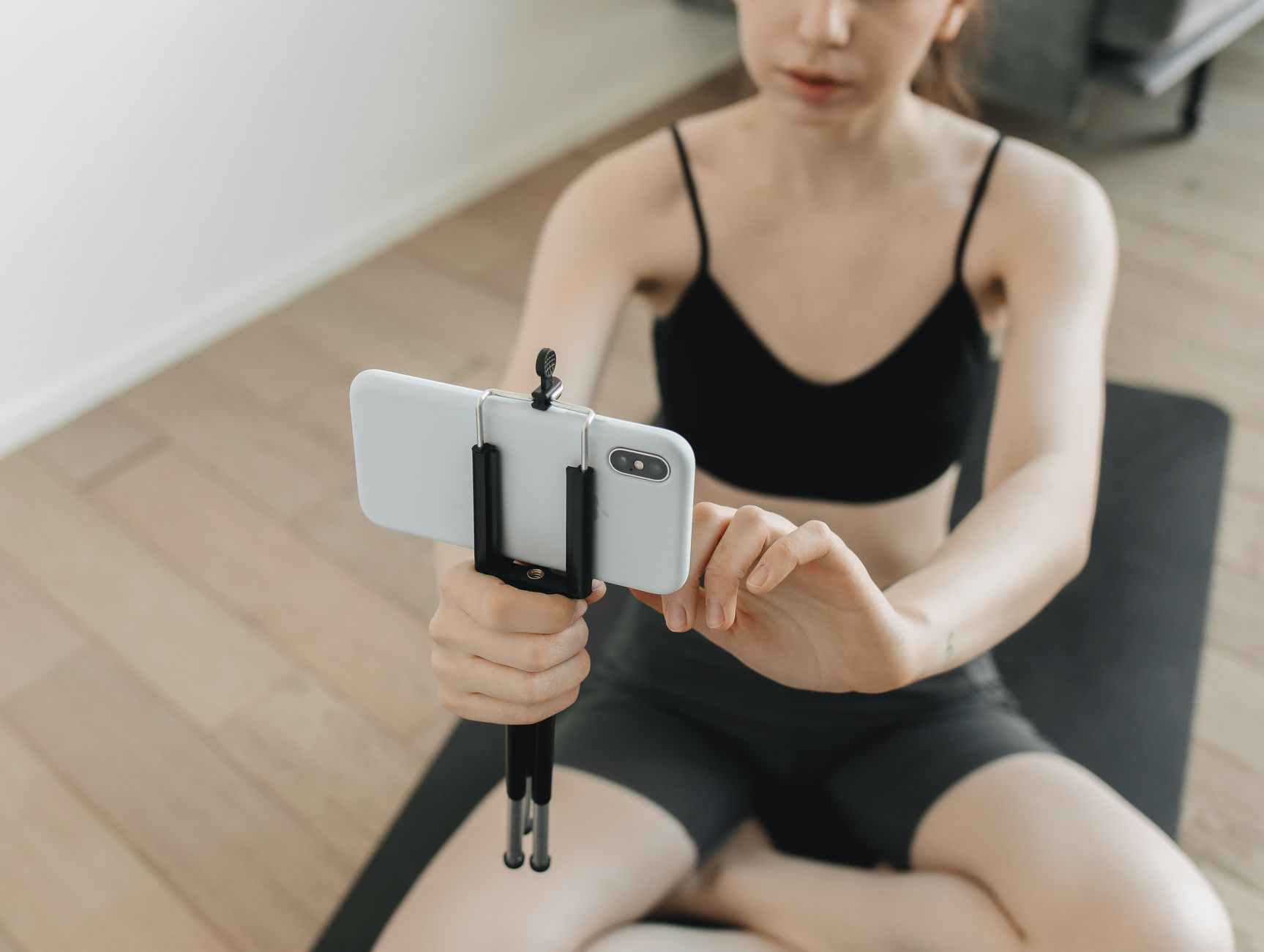 A woman using a smartphone on a tripod to film her yoga session indoors.