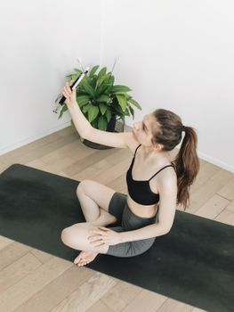 A woman in activewear takes a selfie on a yoga mat indoors, embracing healthy living.