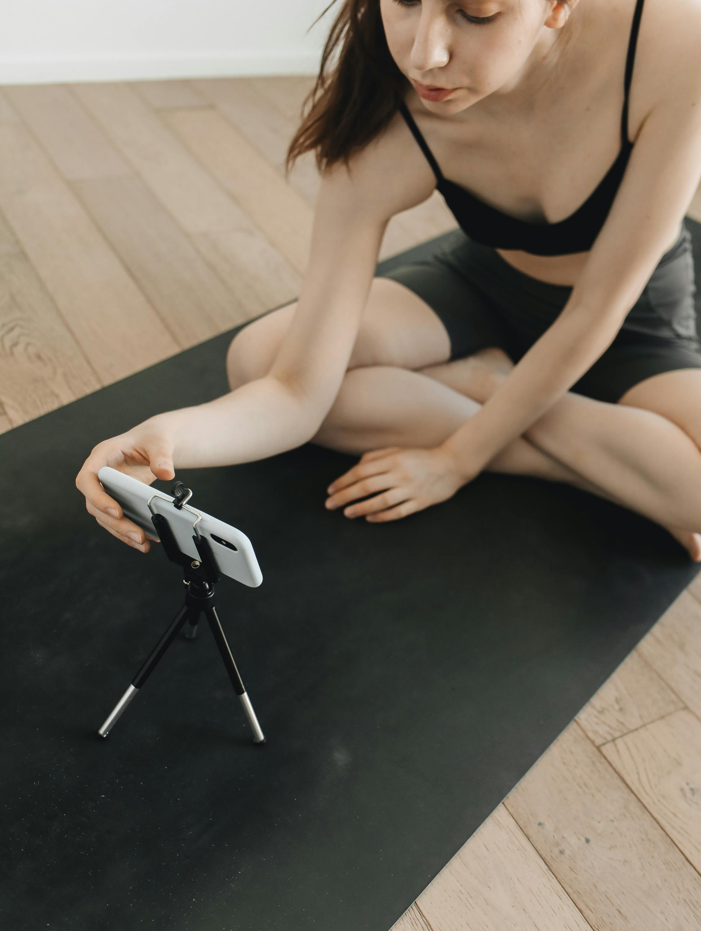 年轻女子在室内用智能手机和三脚架录制视频的同时练习瑜伽