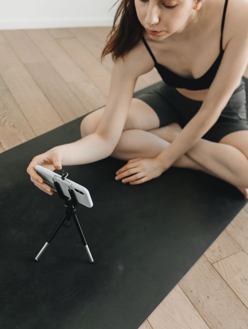 Free Young woman practicing yoga while recording a video indoors using a smartphone and tripod. Stock Photo